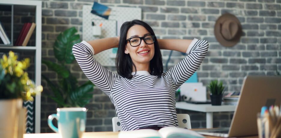 a woman sitting at a desk with her hands behind her head